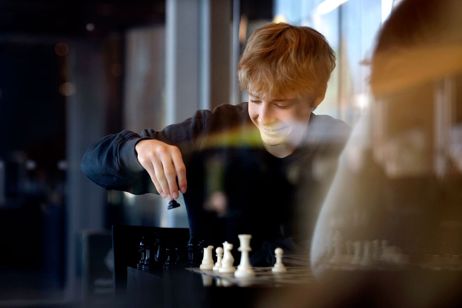Nuori poika hymyilee ja pelaa shakkia, kuvituskuva.