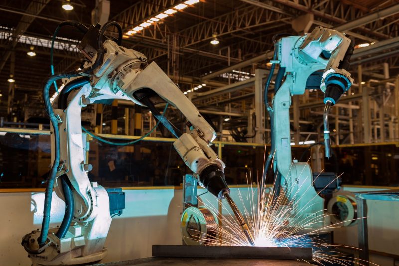 Kaksi isokokoista teollisuusrobottia työstää metallia.
